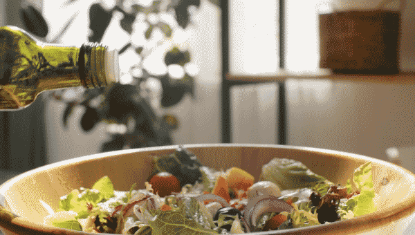 Olive oil being poured into a bowl full of salad