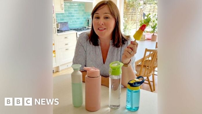 Catherine Burne holds an ice lolly in a kitchen with water bottles