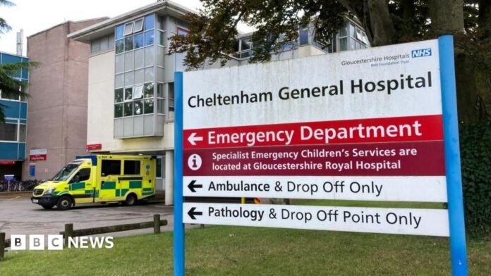 The sign for Cheltenham General Hospital's Emergency Department on a grass lawn in front on the main building, next to a parked ambulance