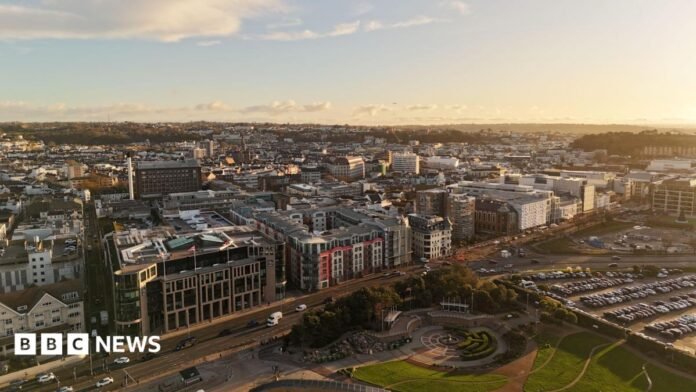 Drone shot of St Helier, Jersey. It shows buildings along a road. Behind there are many more buildings stretching off into the distance. 