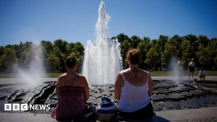 Two women look at a fountain on a sunny day with their backs to the camera