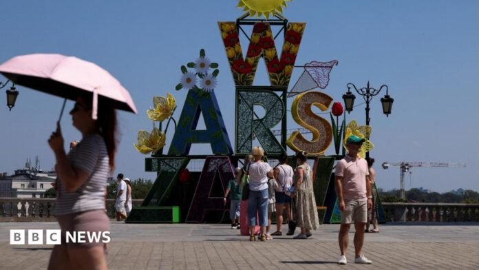A woman walks under an umbrella past a "Warsaw" sign as a heatwave sweeps Poland, in Warsaw, Poland, 