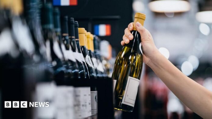 A person takes a glass bottle of wine off of a supermarket shelf