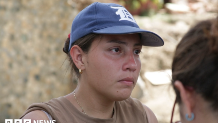 Andreina Valerio, in a blue baseball cap, stands in front of rubble