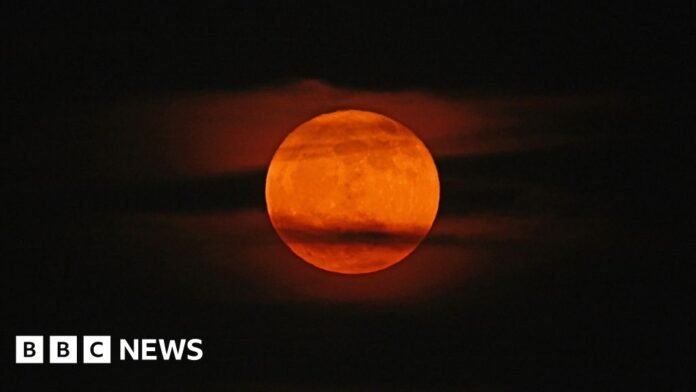 A strawberry moon in the night sky, seen through wisps of cloud.