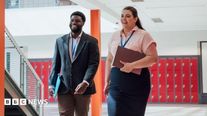 Two employees walk together while smiling. They're both wearing lanyards and holding folders.  