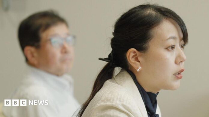 Shoko Kawata, a female mayor in a white blazer and dark blouse sits on an armchair. Her deputy in a light-coloured shirt is visible behind her. 