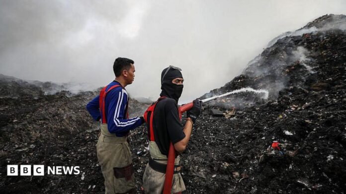 Two people spray water onto large smouldering hillsides