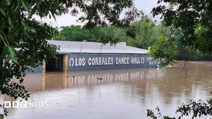 Floodwaters are seen engulfing the Rodeo Los Corrales Dance Hall in Comfort. Trees sit around the hall. 