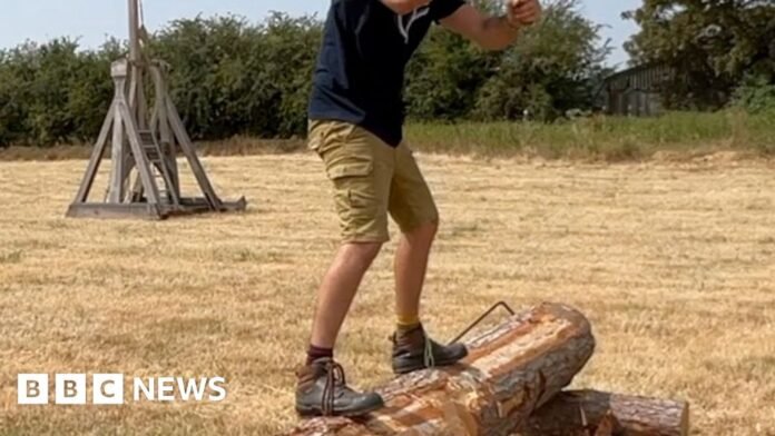 A man stands on a log holding an axe.