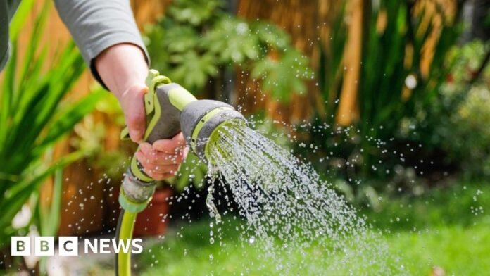 A hand holding a hosepipe spraying water