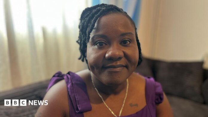 Christiana Hansen is looking straight into the camera, she is sitting on a sofa in her living room. She is wearing a purple dress and a gold chain.