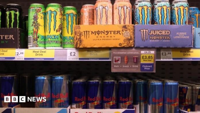 Brightly coloured Monster energy drinks are displayed on a supermarket shelf above rows of Red Bull cans. Several signs show the drinks are on offer as part of a meal deal