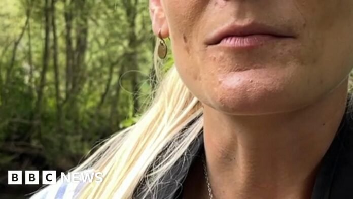 A woman wearing a life jacket is standing in a stream, she has blonde hair.