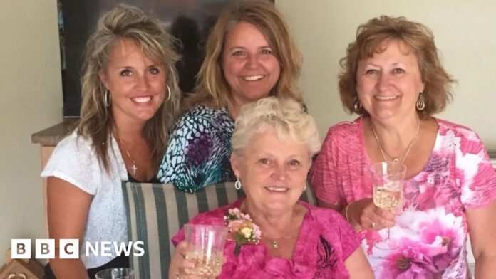 Anita LeBrun, 82, wears a bright pink floral top and corsage, smiling as she holds up a glass of white wine as female members of her family stand around her