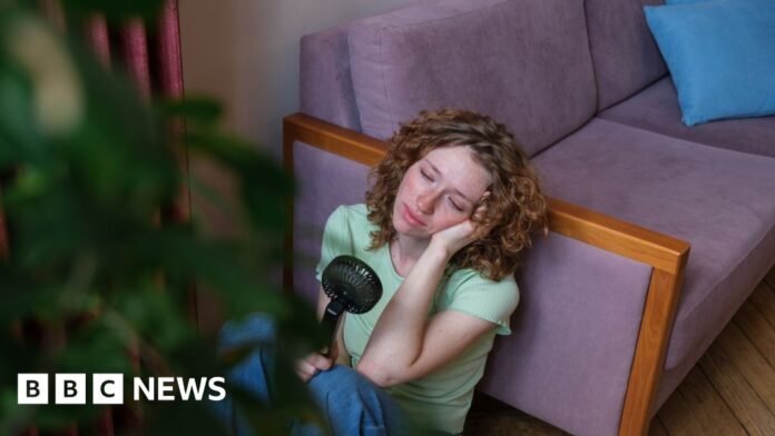 A woman with shoulder-length curly hair leans on a couch while holding a fan
