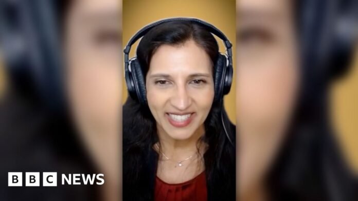 A woman with long dark hair, wearing radio headphones and a red top, smiles into the camera.