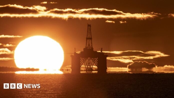 The sun on he horizon behind an oil and gas platform in the North Sea. The sea is calm and the whole scene is a vivid orange colour.