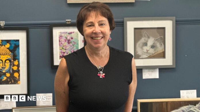 Dr Nicola Fox is stood, smiling, with a gallery of art behind her
