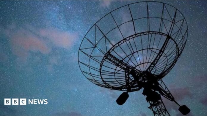 A radar disc pointed a dark night sky with an array of stars and clouds, tinged in purple, visible. The radar itself is in silhouette
