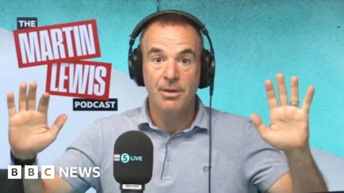 Martin lewis has short day hair, is wearing headphones and a blue polo-shirt and had his hands up to the side of him.