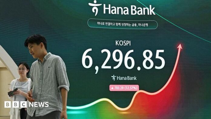 A man and a woman walk past an electronic screen showing 31 July's Kospi trading figures 
