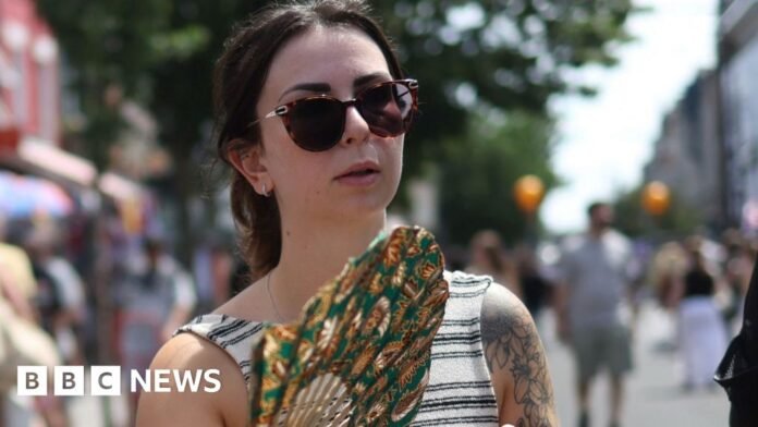 Woman in stripy top and sunglasses carrying a fan