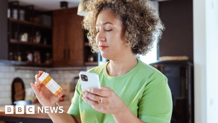 Woman checking prescription bottle while holding her smartphone at home