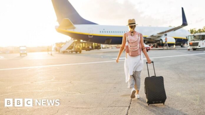 A woman with a suitcase walks towards a passenger aeroplane
