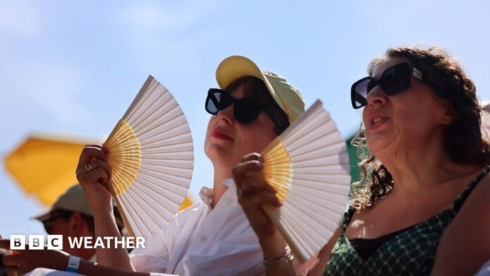 Two women in sunglasses fan themselves, with blue sky and sunshine overhead