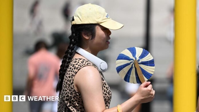 A woman cools herself with a handheld fan whilst walking in the street. 