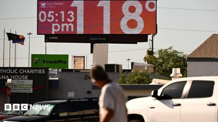 Man walks through road and looks up at sign that says 118 degrees and 05:15 pm