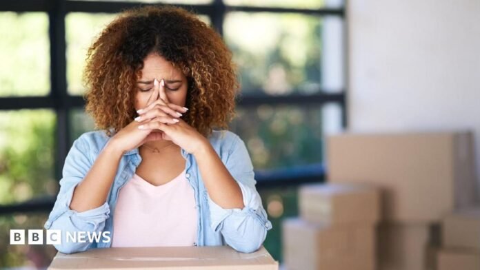 A woman with her head in her hands surrounded by boxes