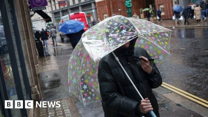 Woman holding spotty open umbrella wearing a dark coat walking on a busy street