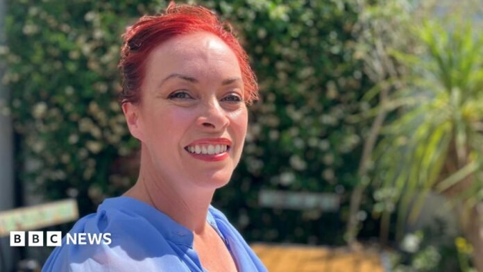 This Morning TV's soap expert Sharon Marshall sits in the sunshine. She is smiling at the camera and is wearing a bright blue blouse. 