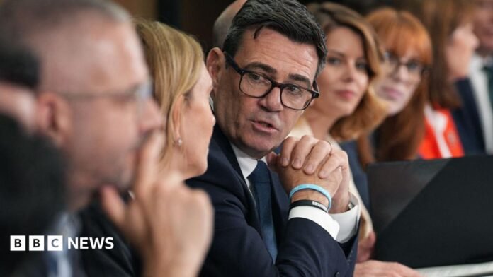 Andy Burnham clasps his hands as he looks towards camera while speaking to others sitting on a long table at a meeting of the National Economic Council in Manchester on 24 July.