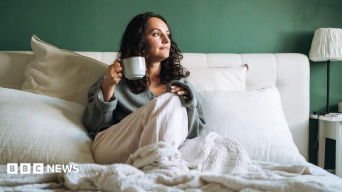 A woman in bed drinking a cup of tea