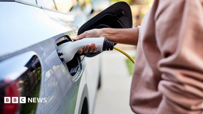 A woman plugs a charging cable into a grey electric car.