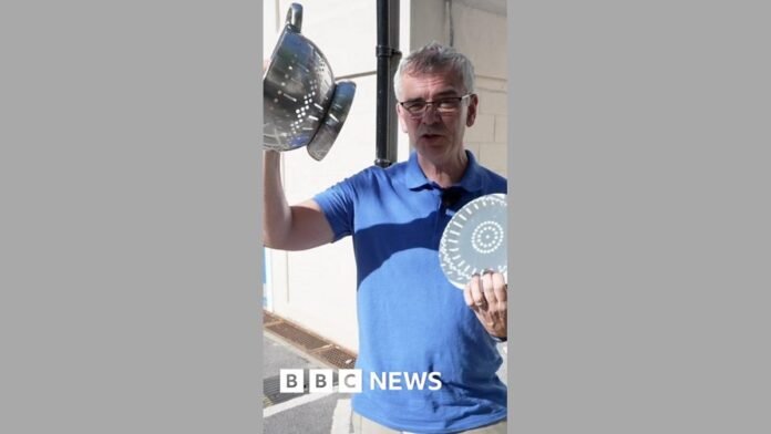 A man holding up a colander and a white paper plate, which has shadows cast on it.