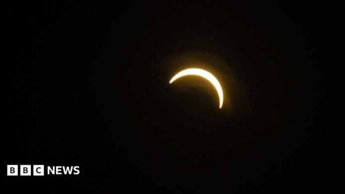 A bright crescent of sunlight appears against a black sky as the Moon passes in front of the Sun during a partial solar eclipse.