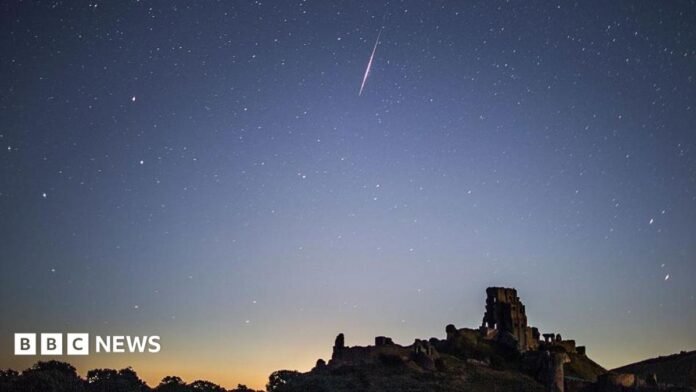 A bright Perseid meteor streaks across a star-filled night sky above the silhouette of Corfe Castle