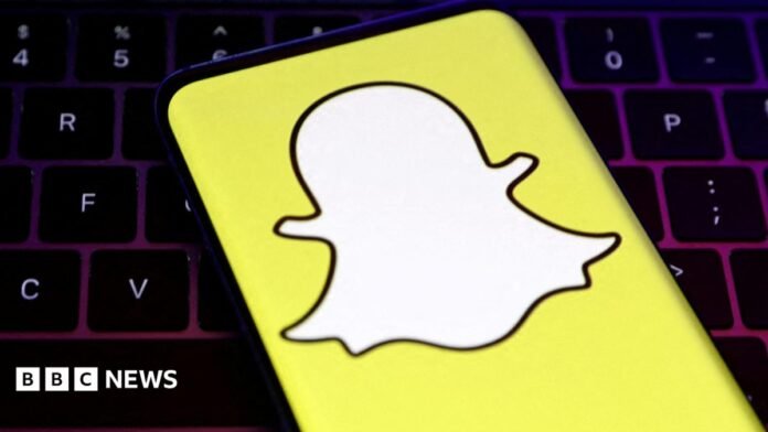 A closeup of Snapchat's logo, a white cartoon ghost with a bright yellow background, held over a laptop conputer keyboard.