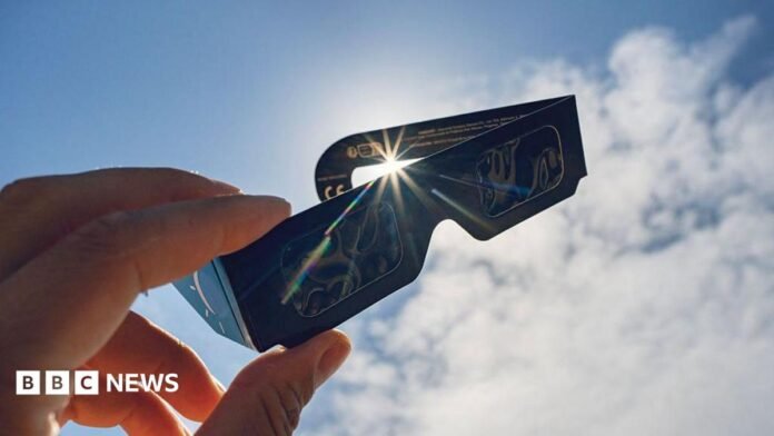 A pair of eclipse glasses held up in front of the sun