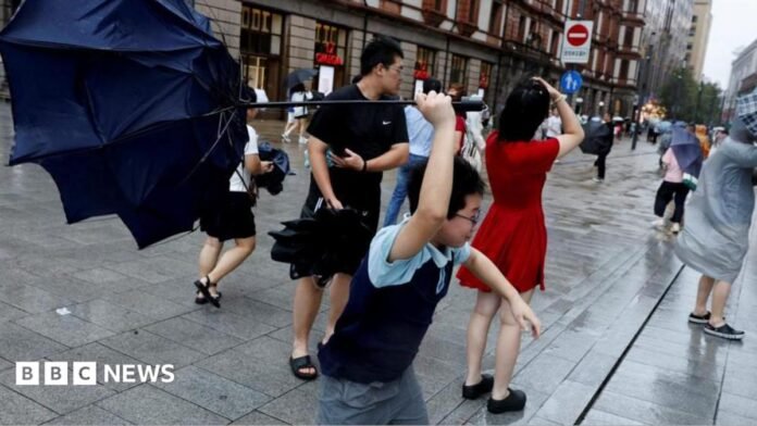 People holding umbrellas along a street in Shanghai. One boy is seen trying to hold on to an inverted umbrella as winds intensify