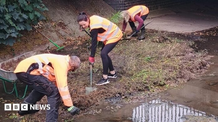 Volunteers in high viz on the floor of a river with almost no water lifting soil and silt